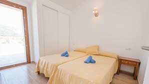 Een kamer met twee bedden, een klein nachtkastje, een wandlamp en een schuifdeur van glas die uitkomt op een buitenruimte.