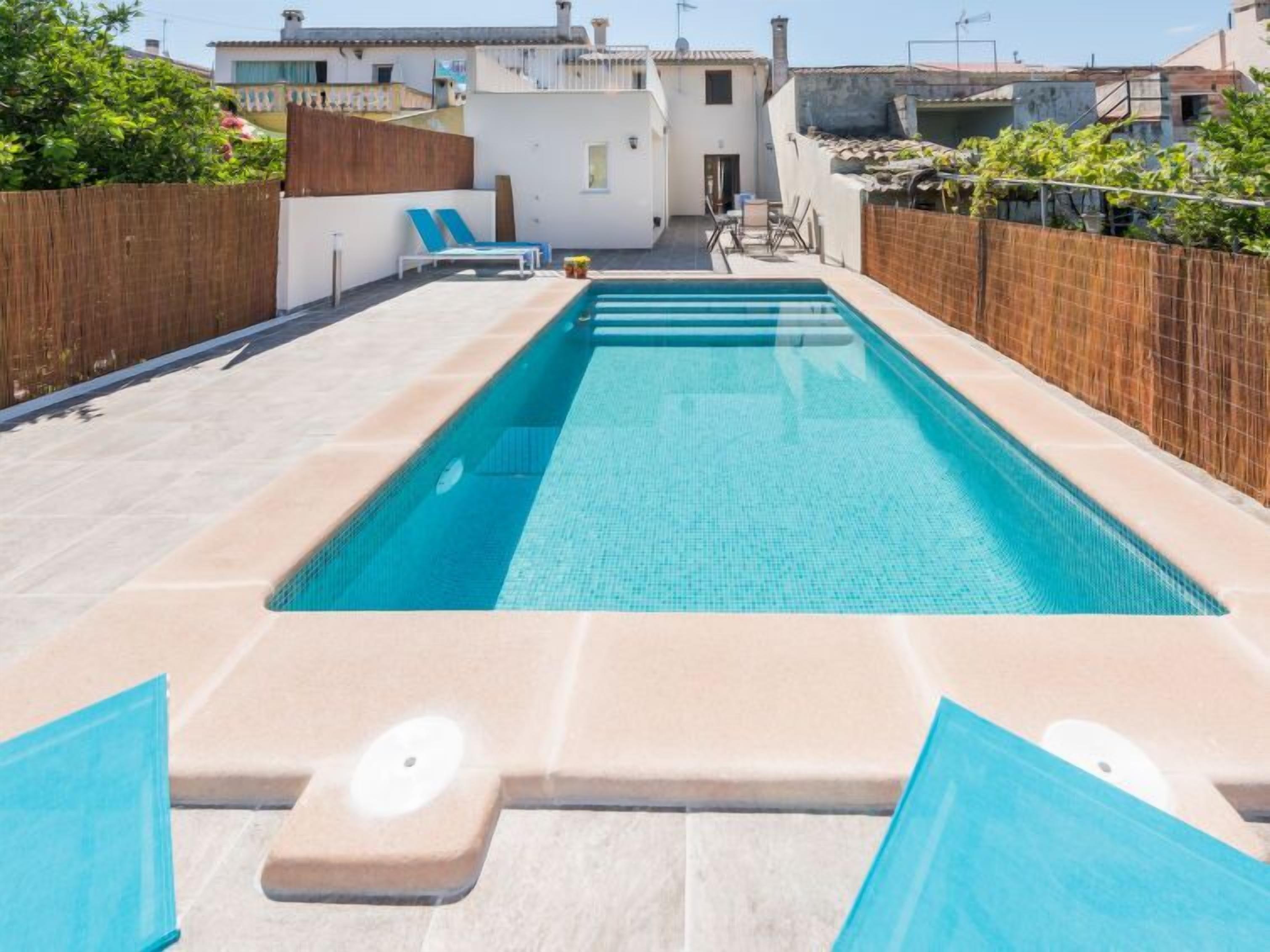 Una piscina rectangular con agua azul cristalina, rodeada por un patio de baldosas.