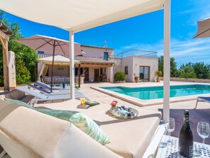 A poolside area with a lounge chair, a table with a bottle and glasses, and a pool. - Vacation home Es Cos by Interhome (Moscari)