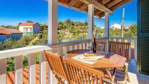 Eine Holzdielen-Terrasse mit Tisch und Stühlen, mit Blick auf eine reizvolle Landschaft mit Häusern und viel Grün.