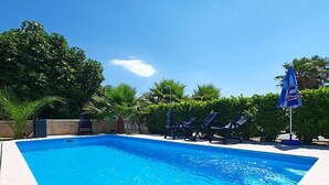 Una piscina con agua azul cristalina, rodeada de sillas de descanso y palmeras.