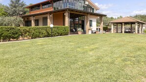 A two-story house with a large glass front, a covered patio, and a well-maintained lawn.