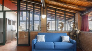 A room with a blue sofa, large windows, and brick walls.