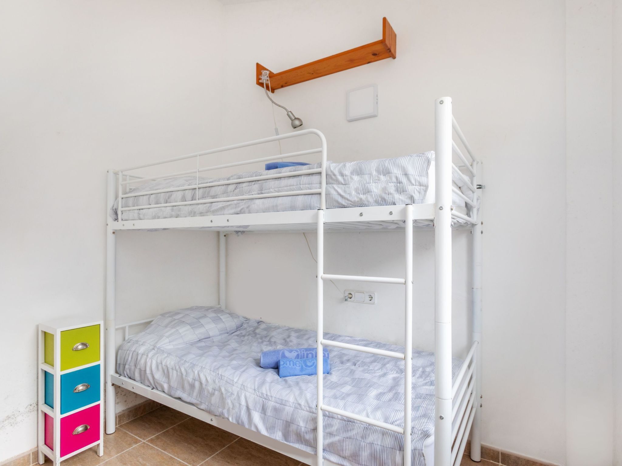 Ein Stockbett mit einer unteren Liege, ein kleines Regal mit Schubladen und ein Holzregal darüber.