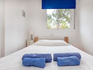 A neatly made bed with white bedding, a nightstand with a lamp, and a window with a view of trees.
