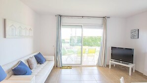 Una sala de estar moderna con sofá, televisor y puertas corredizas de vidrio que dan a un espacio exterior.