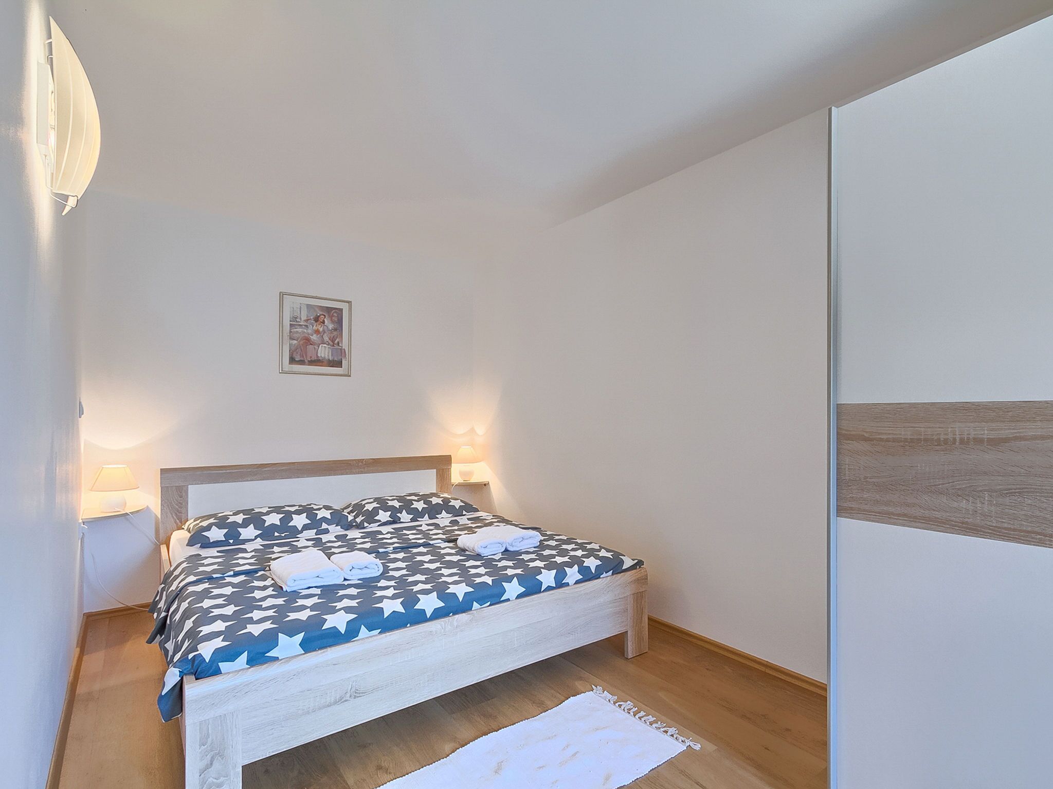 A neatly made bed with a star-patterned bedspread, two bedside lamps, and a small framed picture on the wall.