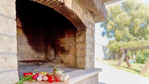 Un horno de piedra al aire libre con una tabla de cortar de madera en primer plano, mostrando verduras frescas.