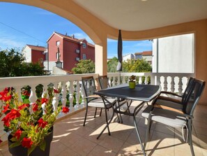 Ein Balkon mit Tisch, Stühlen und einem Blumentopf, mit Blick auf Gebäude im Hintergrund.