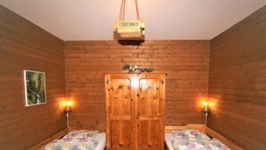 A room with two single beds, wooden walls, a wooden wardrobe, and two wall-mounted lamps. - Vacation home Amberg by Interhome (Schwoich)