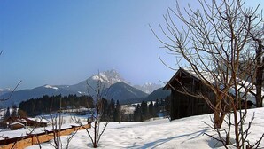 A snow-covered landscape with a mountain in the background, a wooden cabin, and bare trees. - Vacation home Amberg by Interhome (Schwoich)