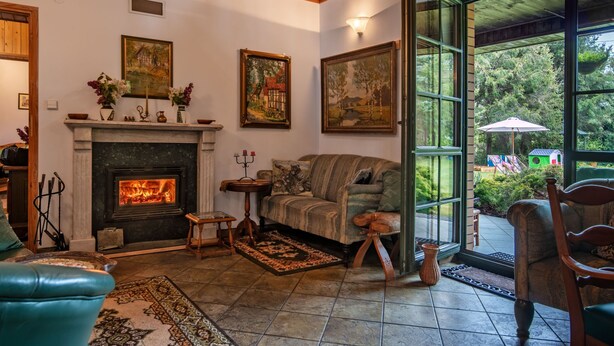 A cozy living room with a fireplace, a sofa, and a view of a garden through large windows. - Modlinek by Interhome (Ustka)