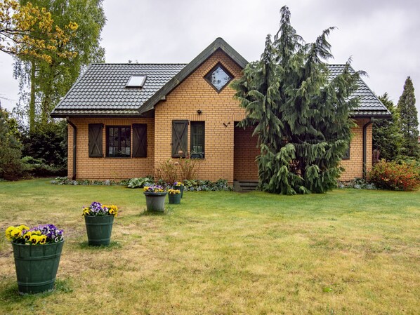 A two-story house with a sloped roof, a small porch, and a well-maintained lawn with flower pots.