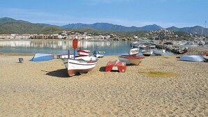 A beach with several small boats parked on the sand, a calm body of water, and a town in the background with mountains. - Niviroma by Interhome (Llançà)