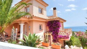 A two-story house with a Mediterranean architectural style, featuring a balcony with purple bougainvillea flowers, a pool area with various plants, and a view of the sea. - Niviroma by Interhome (Llançà)