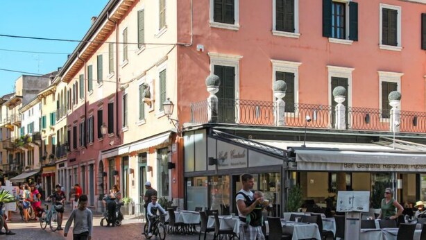 A cobblestone street with outdoor seating at a restaurant, surrounded by historic buildings with balconies and shutters. - Rondinelli by Interhome (Peschiera del Garda)
