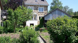 Een stenen huis met een tuin, een tuinhuisje en een heldere lucht.