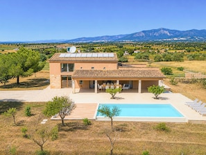 A modern two-story house with a swimming pool, surrounded by a rural landscape and mountains.