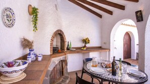 Uma área de refeições rústica ao ar livre, com forno de pedra, vigas de madeira e piso de azulejos.