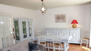 Ein Wohnzimmer mit einer Couch, einem Esstisch mit Stühlen, einem Schrank und einer roten Lampe.