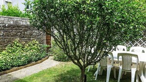 Ein Garten mit Baum, Steinmauer sowie weißen Plastikstühlen und -tisch.