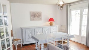 Ein Essbereich mit einem weißen Tisch und Stühlen, einer roten Lampe auf einem weißen Schrank und einem Gemälde an der Wand.