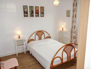 A bedroom with a wooden bed, white bedding, two bedside tables with lamps, a small chair, and a floral curtain.