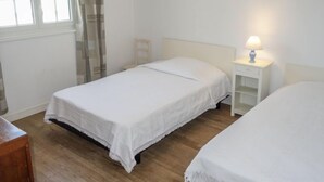 Ein Schlafzimmer mit zwei Einzelbetten, einem Nachttisch mit Lampe, einem Sessel und einem Fenster mit Vorhängen.