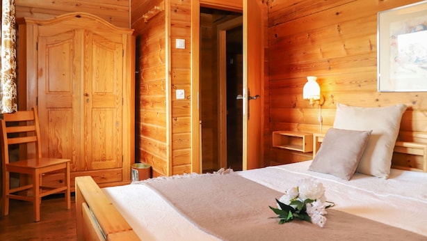 A wooden cabin bedroom with a bed, bedside table, lamp, and a chair. - Château Lapin by Interhome (Verbier)