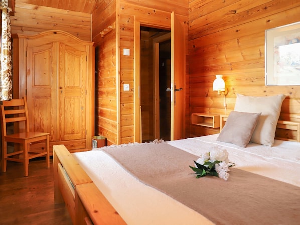 Camera da letto in una baita di legno, con un letto, un comodino, una lampada e una sedia.