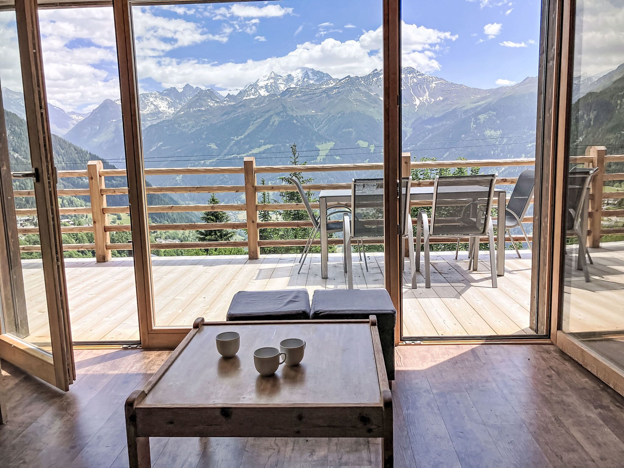 A wooden deck with a table and chairs, overlooking a mountainous landscape.