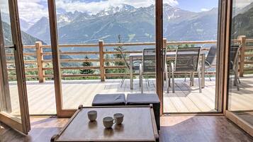 Una terrazza in legno con tavolo e sedie, affacciata su un paesaggio montuoso.
