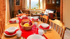 A wooden dining room with a table set for four, featuring red napkins, white plates, and a basket of fruit. - Château Lapin by Interhome (Verbier)