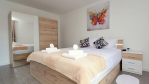 Une chambre à coucher moderne avec un lit en bois, une literie blanche et un tableau coloré représentant un papillon accroché au mur.