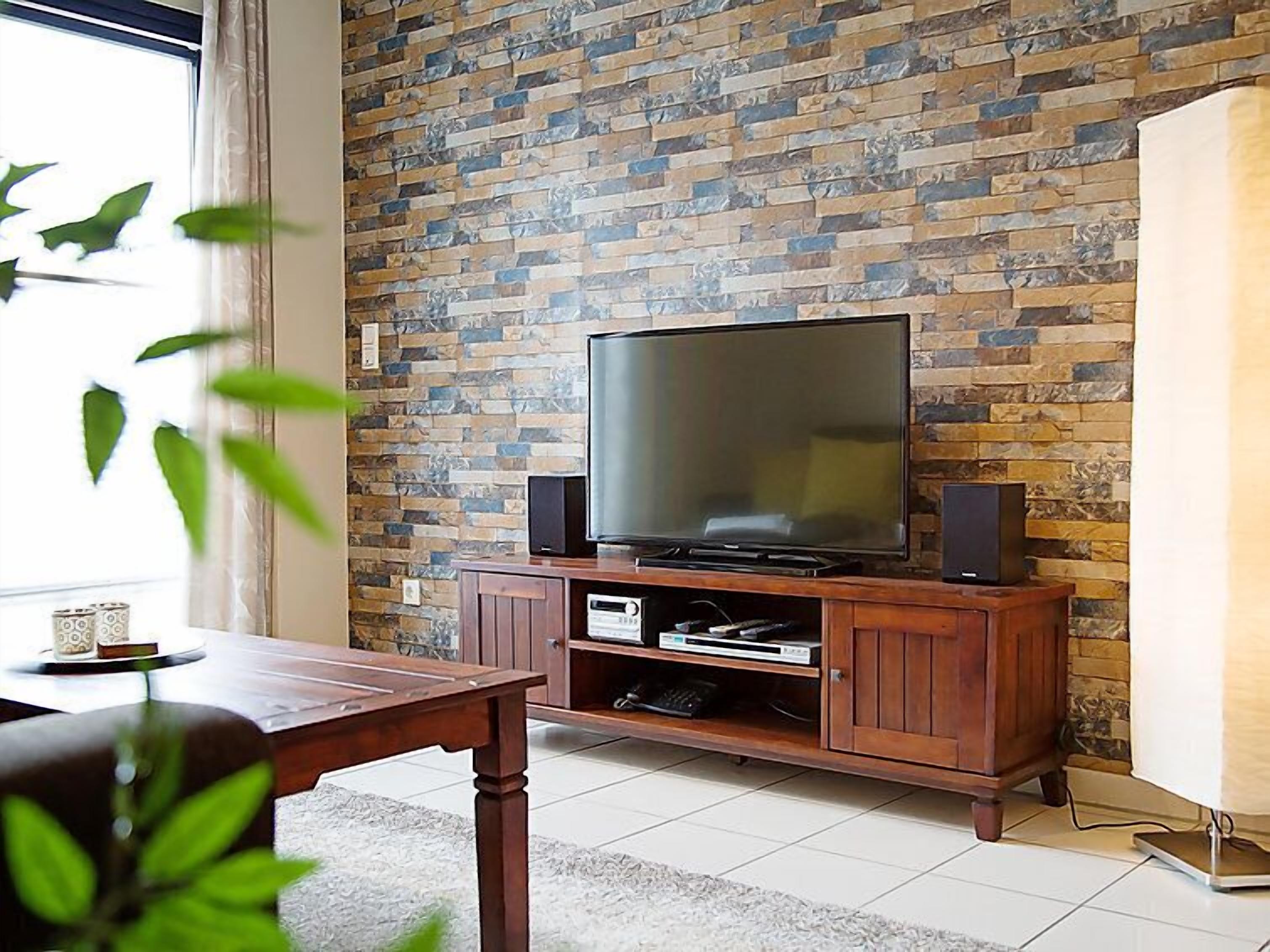 Un salon avec un mur en pierre, un téléviseur à écran plat posé sur un meuble en bois et une table à manger avec des chaises.