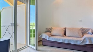 A modern living room with a sliding glass door leading to a balcony, a sofa with patterned cushions, and a small table.