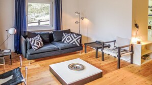 Ein modernes Wohnzimmer mit grauem Sofa, gemusterten Kissen, einem Couchtisch, einem Beistelltisch und einer Stehlampe.
