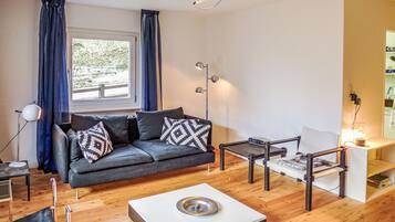 Ein modernes Wohnzimmer mit grauem Sofa, gemusterten Kissen, einem Couchtisch, einem Beistelltisch und einer Stehlampe.