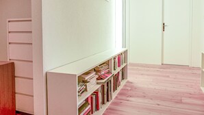 Ein Flur mit einer weißen Tür, einem weißen Bücherregal voller Bücher und einer weißen Wand.