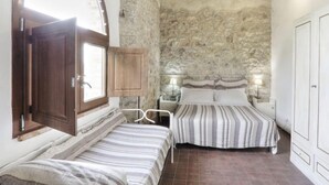 Une chambre avec deux lits, des murs en pierre, des poutres en bois et une fenêtre avec un cadre en bois.