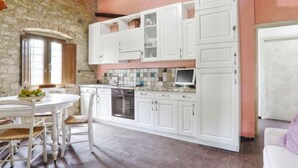 Une cuisine avec des meubles blancs, un pare-feu en carreaux et un coin repas comprenant une table et des chaises blanches.