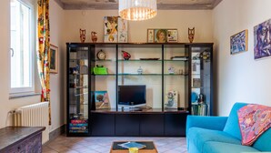 A living room with a TV, a blue sofa, a coffee table, and a bookshelf filled with various items.