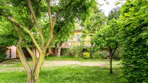 A lush garden with mature trees and a yellow building in the background.