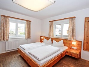 A double bed with wooden headboard and nightstands, two windows with curtains, and a radiator.