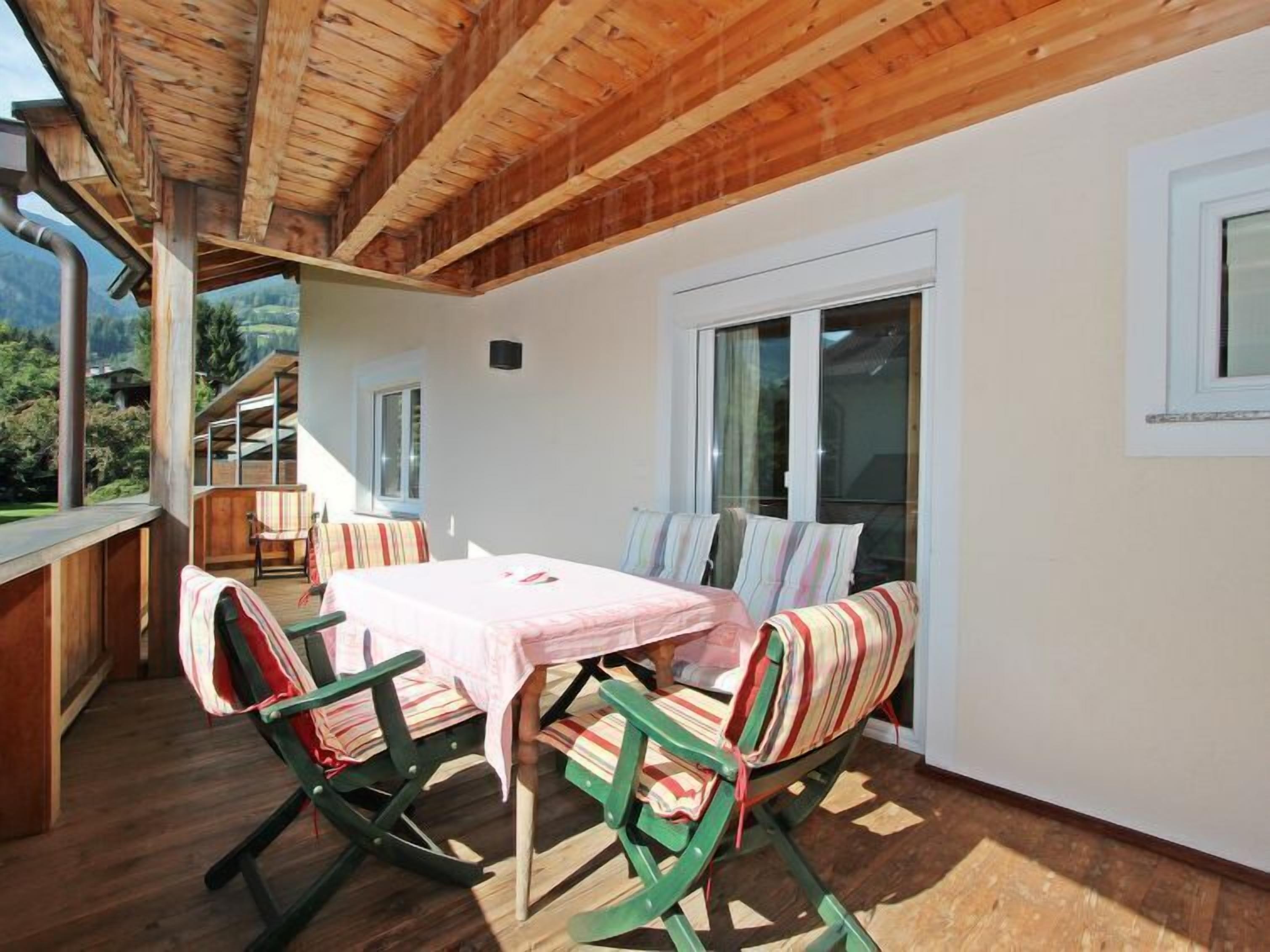 Uma área de estar aconchegante ao ar livre, com mesa e cadeiras, teto de madeira e vista para as montanhas.