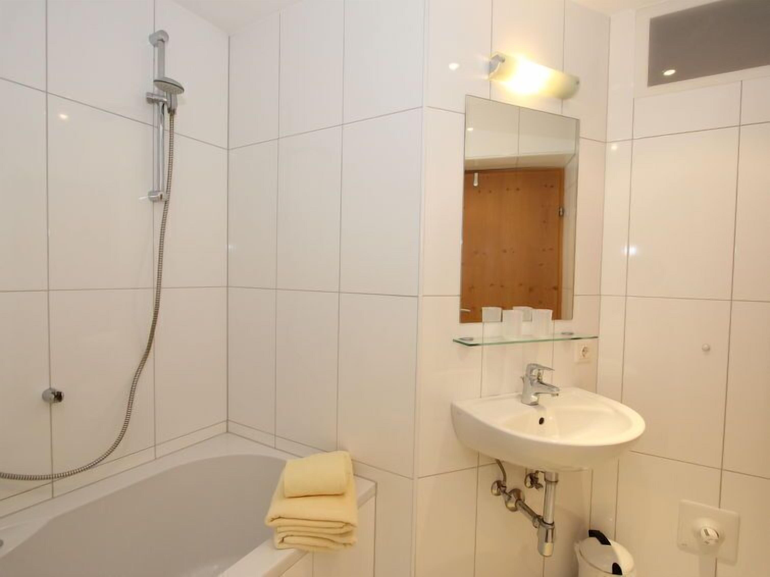 A modern bathroom with a bathtub, a glass shelf above the sink, and a showerhead.