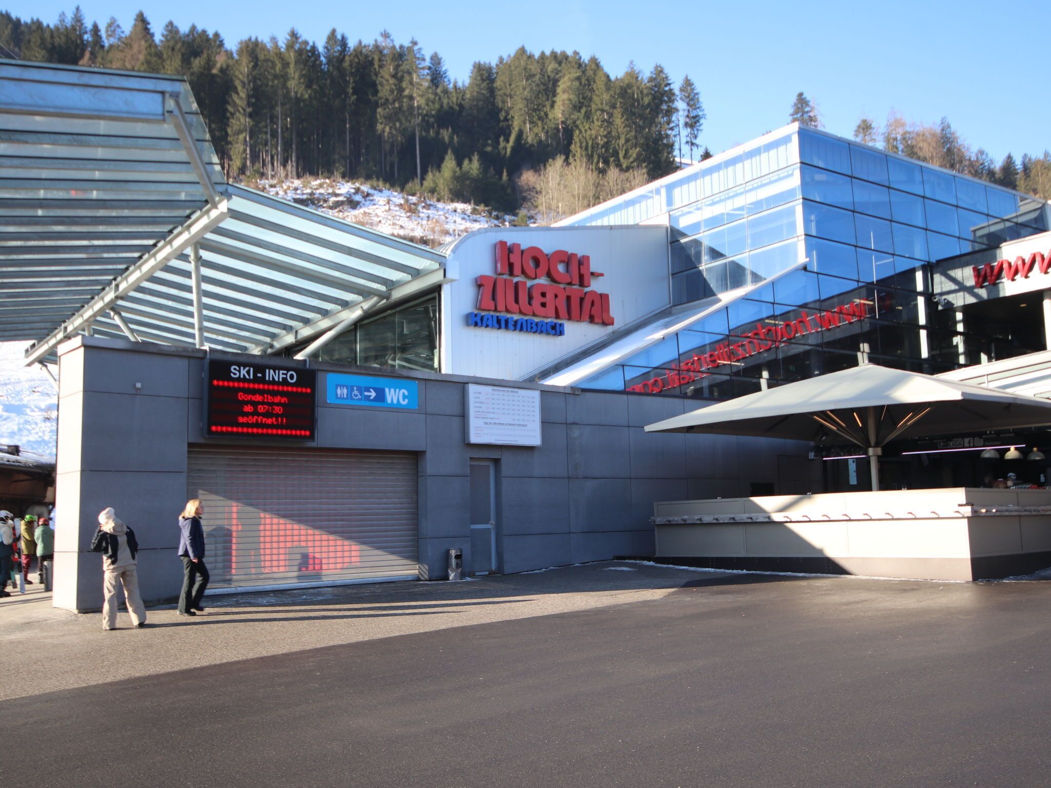 A modern building with a ski information sign, a WC sign, and a large glass facade.