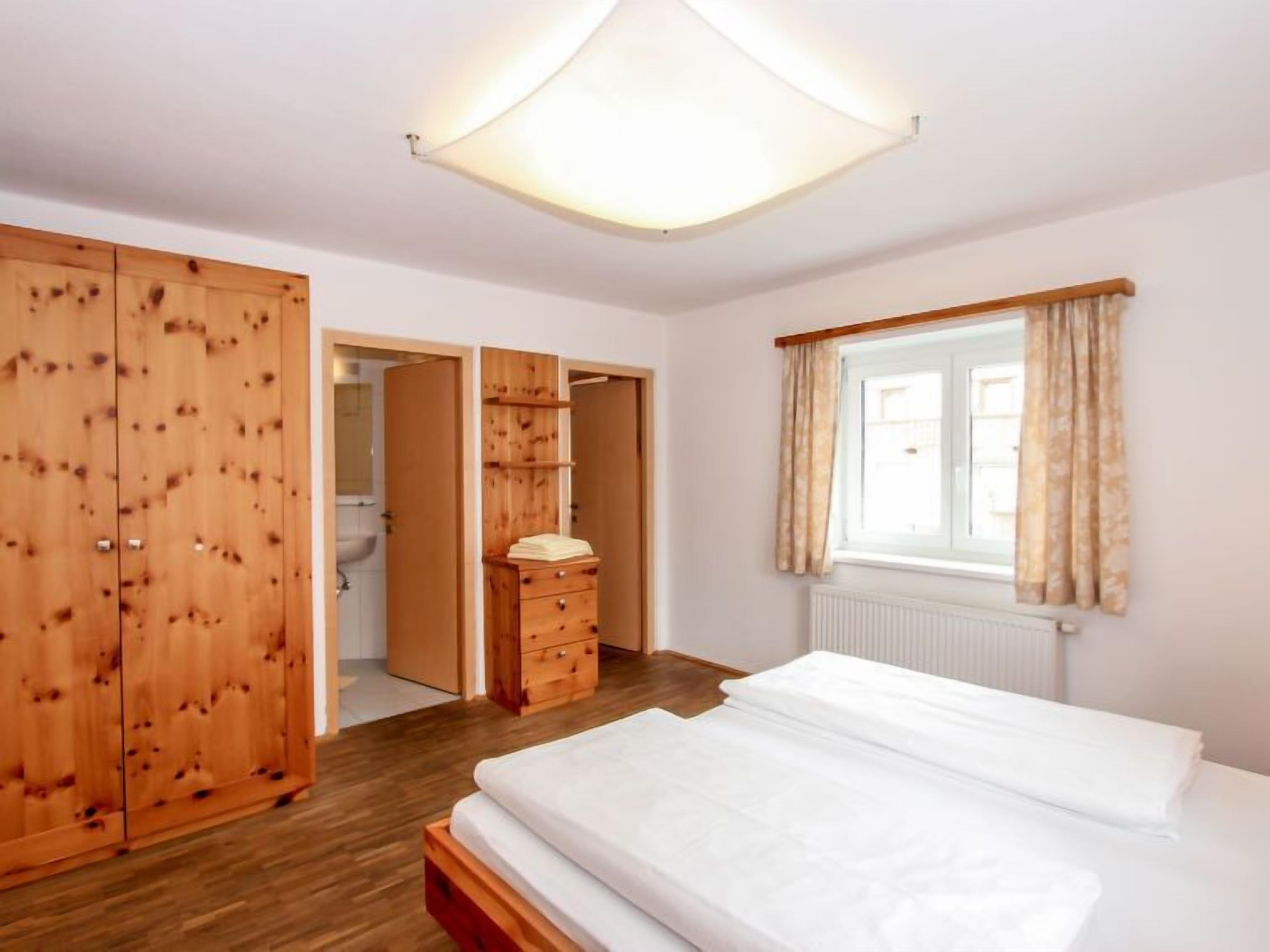 Un dormitorio con un armario de madera, una cama, una ventana con cortinas y una lámpara en el techo.