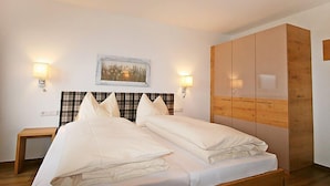 Een slaapkamer met een groot bed, twee bedlampjes, een ruitjes hoofdeinde, een houten garderobe en een ingelijst kunstwerk aan de muur.