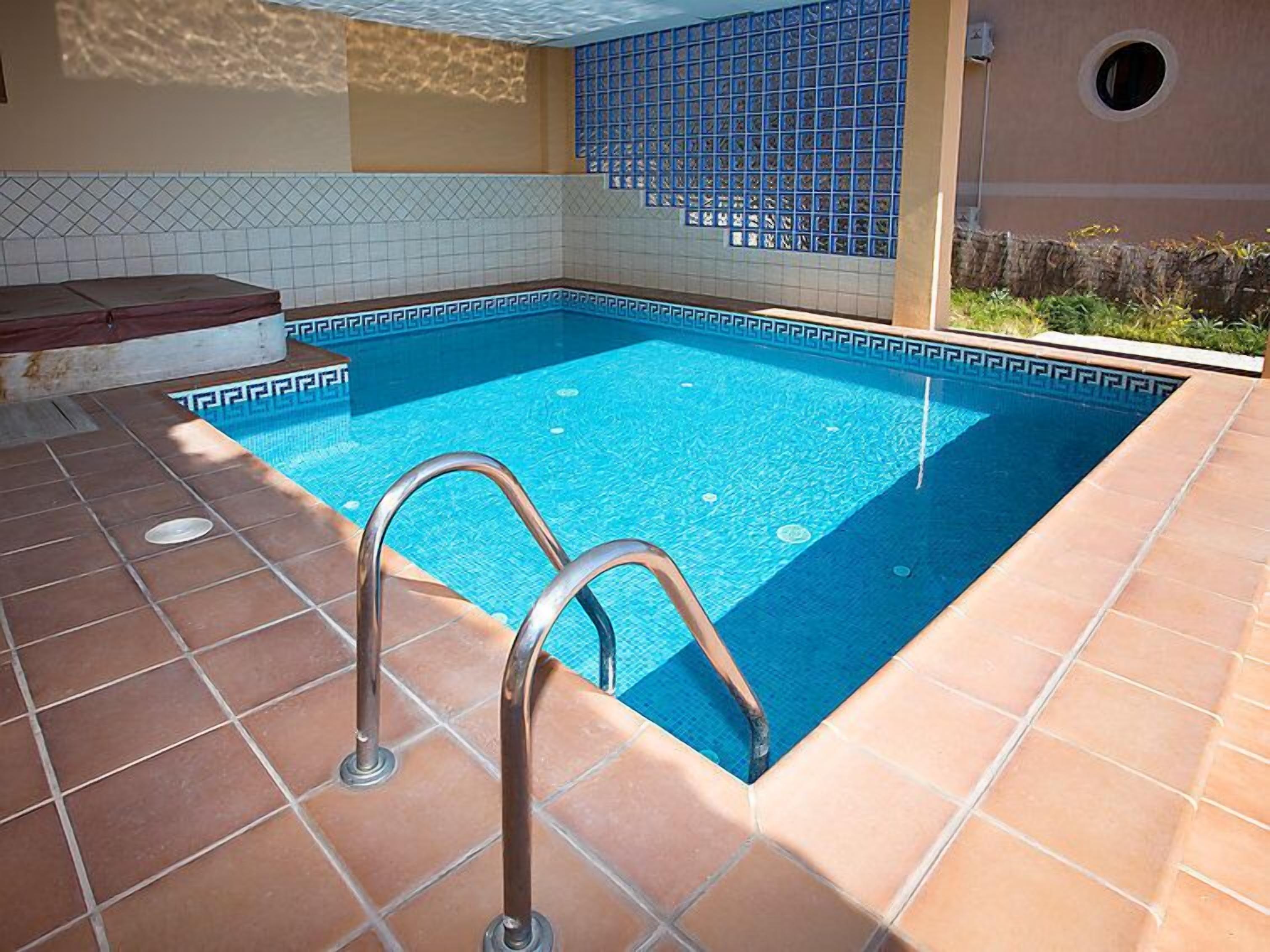 Una piscina con solárium empedrado y escalera metálica.